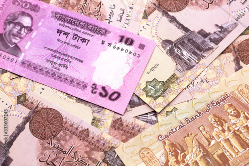 A close up image of a pink, ten taka bank note from Bangladesh on a bed of Egyptian one pound bank notes in macro