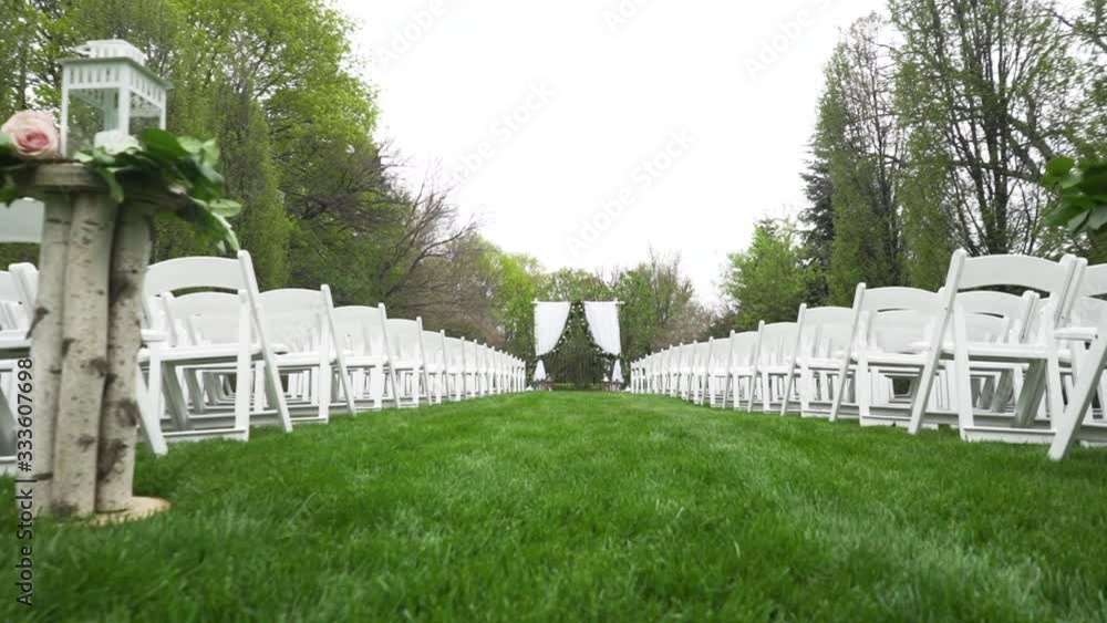 Low angle outdoor wedding aisle ceremony set up no people green trees forest white chairs sunny day Low angle outdoor wedding aisle ceremony set up no people green trees forest white chairs sunny day