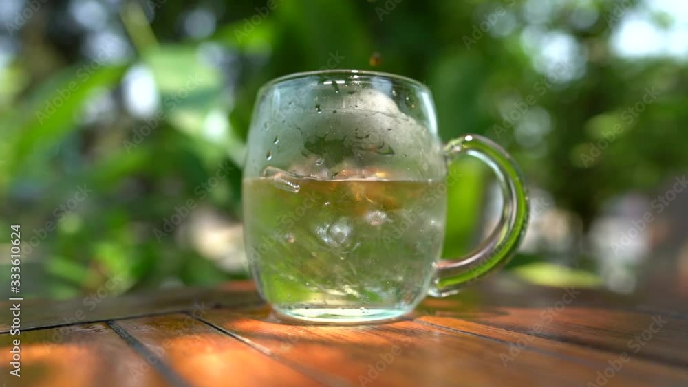 pouring light coffee in glass mug of water on wooden table and green street back ground stock footage slow motion pouring light coffee in glass mug of water on wooden table and green street back ground stock footage slow motion