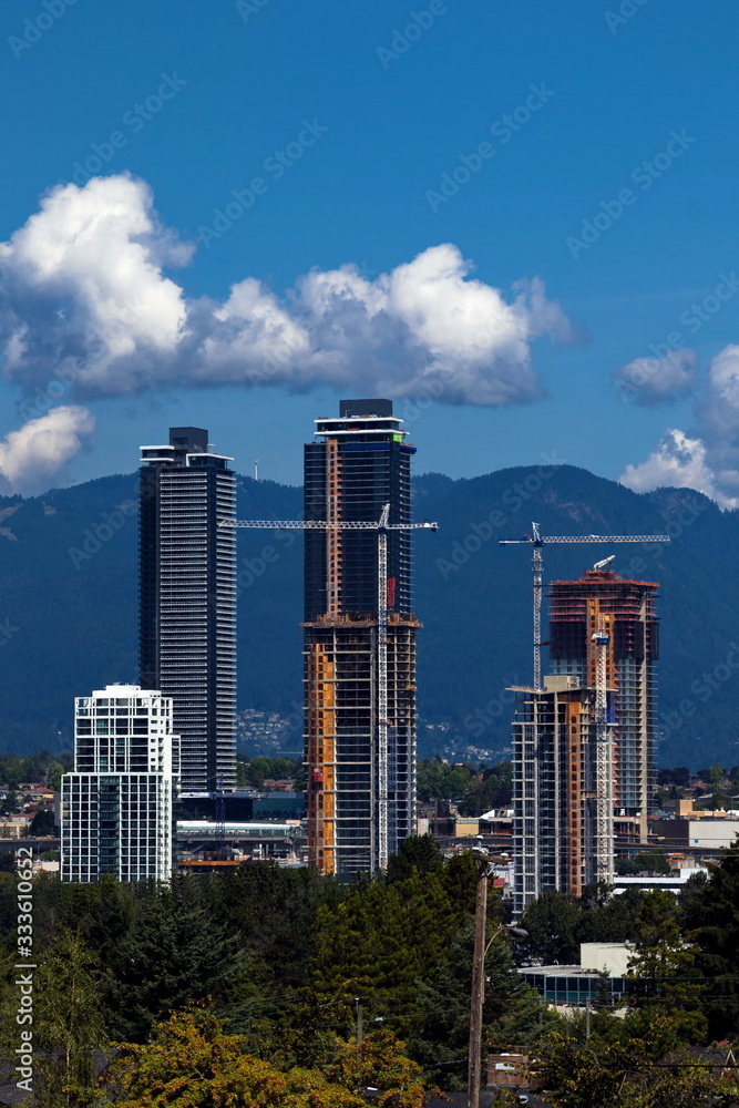 Construction of new high-rise buildings in residential district in the city of Burnaby, construction site, new high-rises and construction cranes against the backdrop of a mountain ridge Construction of new high-rise buildings in residential district in the city of Burnaby, construction site, new high-rises and construction cranes against the backdrop of a mountain ridge