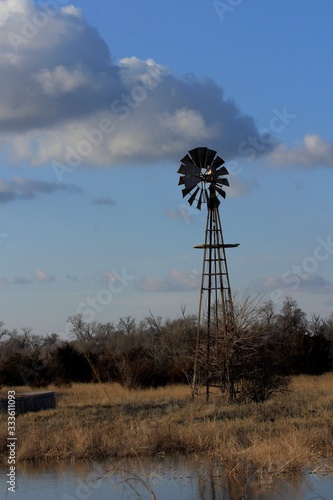 Windmill in a Kansas pasture at Sunset with clouds water, and tree's out in the country.