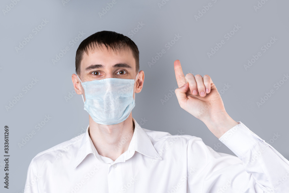 Man in a medical mask. A handsome dark-haired man in a white medical uniform, shirt and medical mask looking at camera and shows a thumbs-up gesture on a gray background. Chinese Coronavirus Man in a medical mask. A handsome dark-haired man in a white medical uniform, shirt and medical mask looking at camera and shows a thumbs-up gesture on a gray background. Chinese Coronavirus