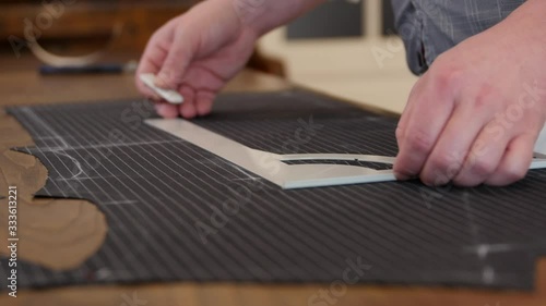 tailor drawing lines on a fabric with his chalk in order to make a bespoke suit-flat profile with anthracite wool made cloth. this stylist working in shop, drawing & cutting templates.