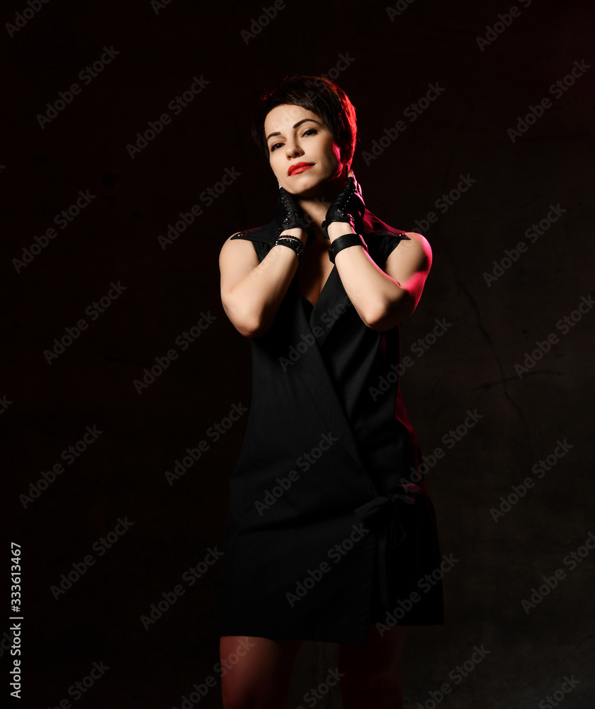 Brunette woman in fashion jacket style dress and leather gloves with cut fingers poses with her hands at her neck Brunette woman in fashion jacket style dress and leather gloves with cut fingers poses with her hands at her neck