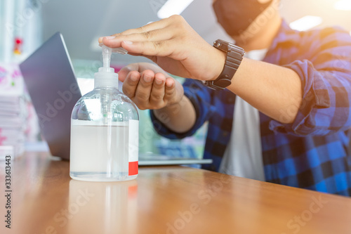 [Coronavirus] Freelance man working from home wearing protective mask. Freelance man in quarantine for coronavirus wearing protective mask. Working from home. Cleaning hands with sanitizer gel.