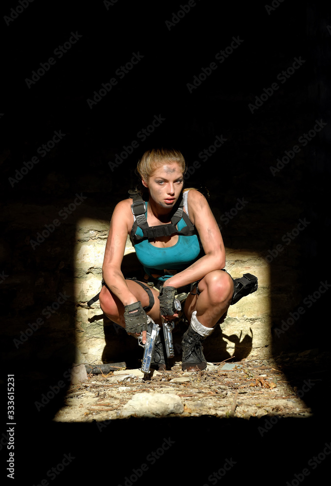 A young woman is dressed up in a military outfit. She crouches down in a dark urban area and observes the scene. She has weapons with her for self defense reasons. A young woman is dressed up in a military outfit. She crouches down in a dark urban area and observes the scene. She has weapons with her for self defense reasons.