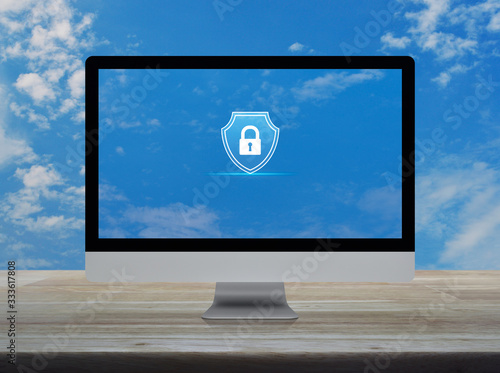 Padlock with shield flat icon on desktop modern computer monitor screen on wooden table over blue sky with white clouds, Business security insurance online concept