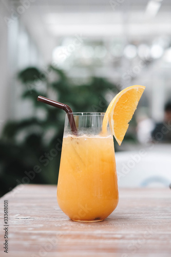Glass of fresh orange juice and  straw on the wooden table in cafe house.
