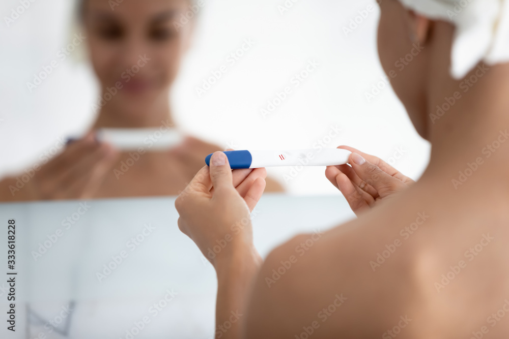 Woman reflected in mirror view over female shoulder, close up focus on hands holds pregnancy test with two red stripes result confirming gestation, rapid detection pregnancy tool advertisement concept Woman reflected in mirror view over female shoulder, close up focus on hands holds pregnancy test with two red stripes result confirming gestation, rapid detection pregnancy tool advertisement concept