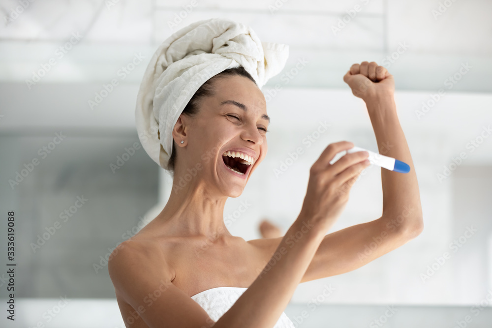Excited woman after shower wrapped in towel standing in bathroom apply rapid detection pregnancy test see two stripes positive result feels happy scream with joy, pregnant female enjoy moment concept Excited woman after shower wrapped in towel standing in bathroom apply rapid detection pregnancy test see two stripes positive result feels happy scream with joy, pregnant female enjoy moment concept