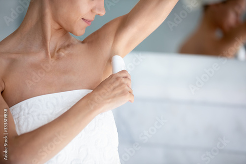 Fototapeta Naklejka Na Ścianę i Meble -  Happy 30s beautiful woman applies antiperspirant stick after shower in morning close up image. Using treatment for bodycare skincare, to reduce sweating, underarm wetness and control body odor concept