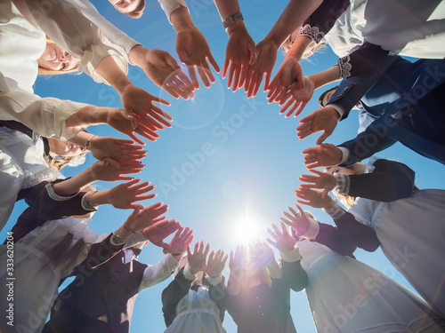 Students graduates make the shape of a circle from the palms of their hands.