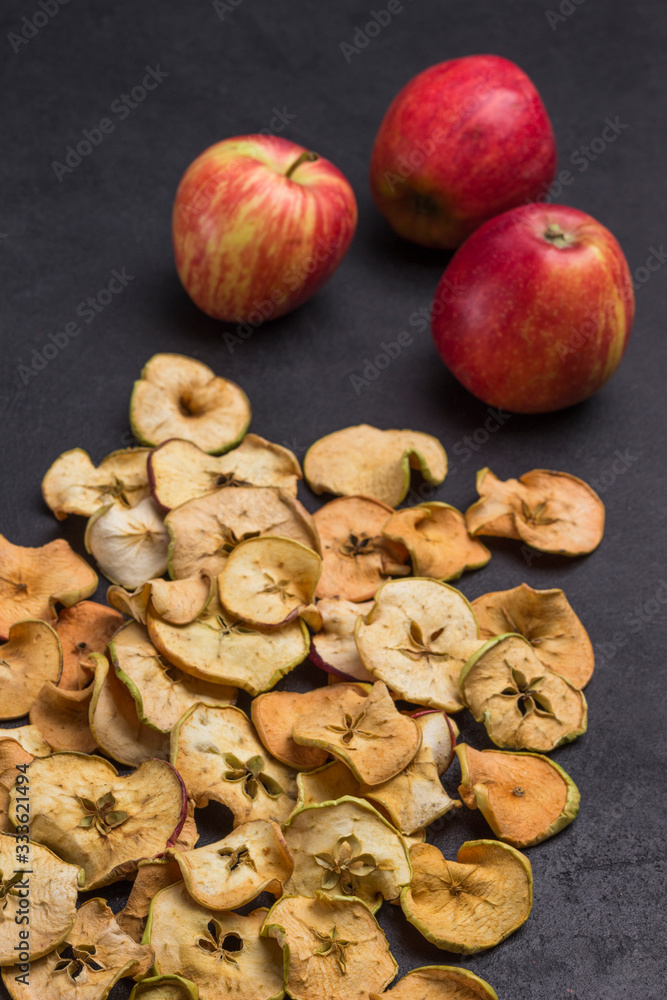 Fototapeta premium Three fresh red apples and slices of dried apples on black background.