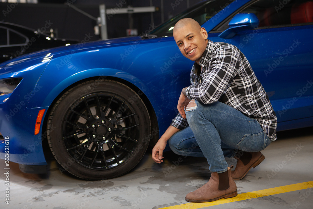 Cheerful attractive African man smiling to the camera while working at his garage with his new sports car