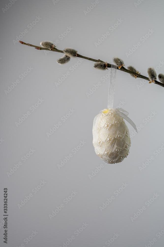 White pearled easter egg hanging from a willow twig with catkins