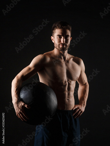 a male athlete in good physical shape on a black background with a medball in his hands