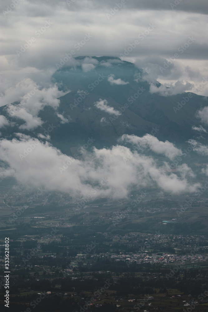 Mountain peak in southern america or Ecuador rising into clouds above green plantations and villages
