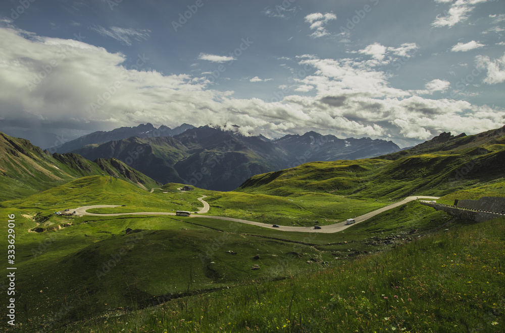 Panorama from Grossglockner pass at Hochtor on a summer day with beautiful clouds, green meadows and winding road seen below. Summer on mountain pass.