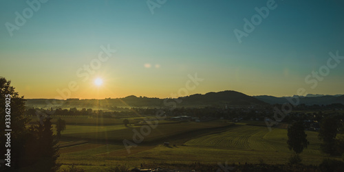 Beautiful morning panorama of a village or city of Sankt Georgen in Attergau  Austria. Visble sun with rays rising above the houses and green meadows.