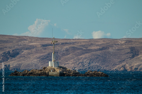 White small lighthouse or beacon on a rock formation or little island in the middle of the sea in front of Pag island in Croatia. Beautiful white light beacon on the middle of the sea.