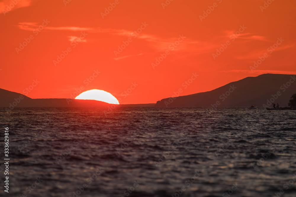 Evening view of croatian coast close to Karlobag with sunset around island of Pag and Rab. Sun just about to set behind two hills into the sea. Evening view of croatian coast close to Karlobag with sunset around island of Pag and Rab. Sun just about to set behind two hills into the sea.