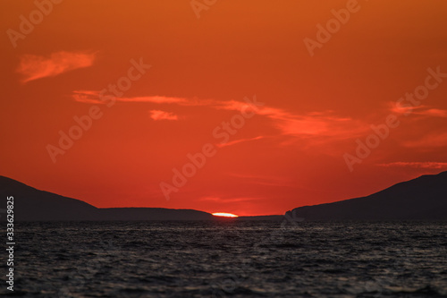 Evening view of croatian coast close to Karlobag with sunset around island of Pag and Rab. Sun just about to set behind two hills into the sea.