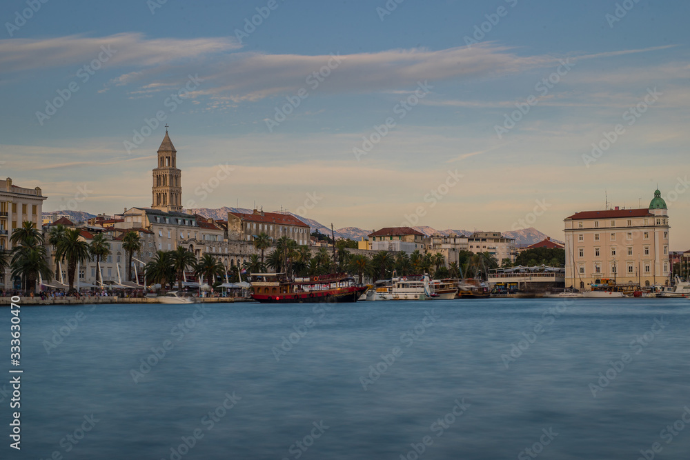 Evening panorama of Split in croata, visible famous Diocletian palace and bell tower. Some ships moored in port, blue and calm evening skies.