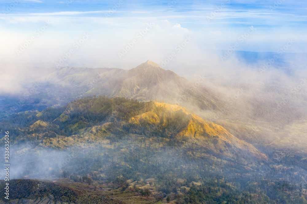 Stunning aerial view of a beautiful mountain range surrounded by clouds during sunrise. Ijen Volcano complex. The Ijen volcano complex is a group of composite volcanoes located in East Java, Indonesia