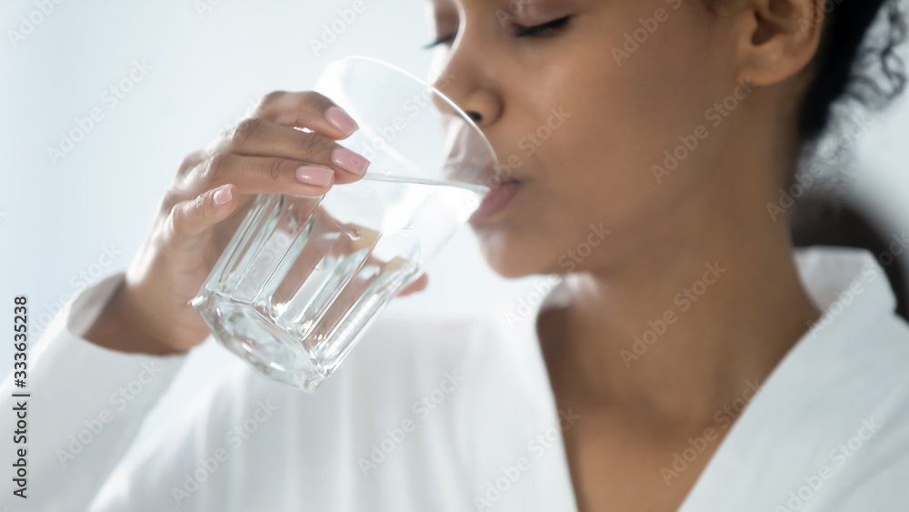 Close up beautiful african woman holding glass drinking a pill with still water. Minerals and vitamins for female, dietary supplement, reducing of thirst, body water balance healthy lifestyle concept Close up beautiful african woman holding glass drinking a pill with still water. Minerals and vitamins for female, dietary supplement, reducing of thirst, body water balance healthy lifestyle concept