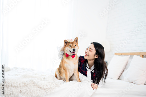 Pet Lover concept. An Asian girl is learning and parody the smile of her Shiba Inu dog. A girl is laying with a Shiba Inu dog on a bed.