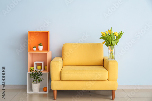Foto Interior of modern room with comfortable armchair, shelf unit and spring flowers