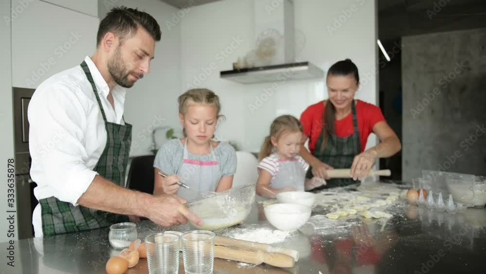Family of four sculpts dumplings in the kitchen. Children help parents. Family of four sculpts dumplings in the kitchen. Children help parents.