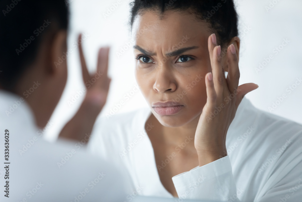 Frown African woman wear white bathrobe looking in mirror see first mimic wrinkles feels stressed, face skin lose elasticity changes after 30s, aging process, need cosmetology facial treatment concept Frown African woman wear white bathrobe looking in mirror see first mimic wrinkles feels stressed, face skin lose elasticity changes after 30s, aging process, need cosmetology facial treatment concept