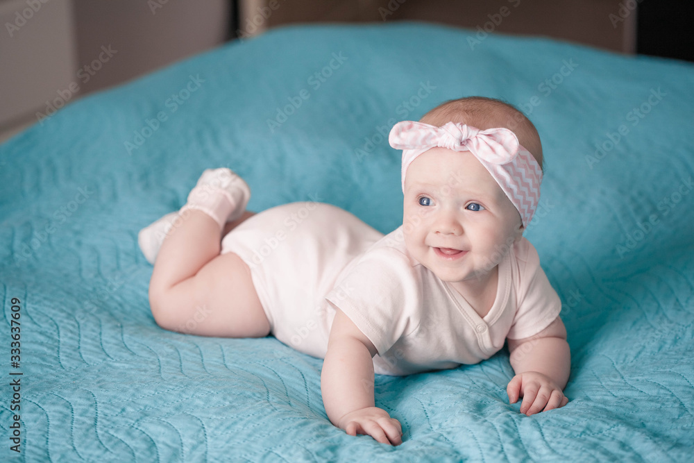 Newborn girl in a headband is lying on a blue blanket and smiling Newborn girl in a headband is lying on a blue blanket and smiling