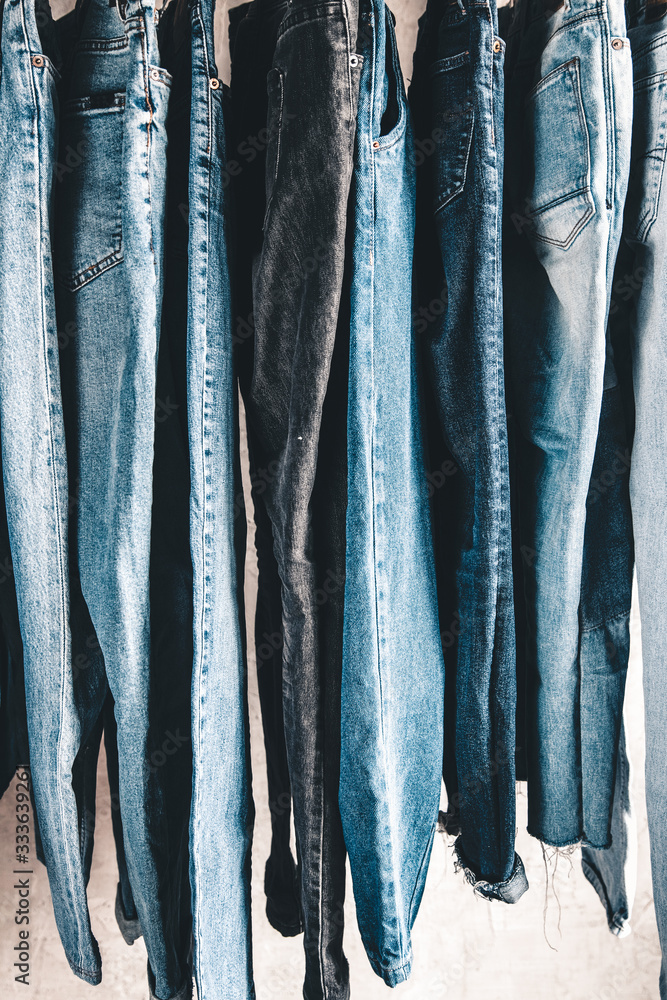 Rack with different jeans on grey background