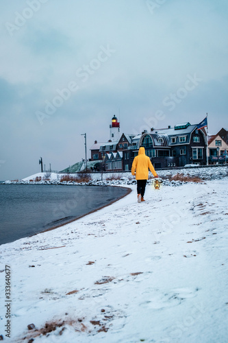 young men in yellow rain jacket walking on a snowy beach by the lighthouse of Urk Netherlands, men with oil lamp and ranin coat photo