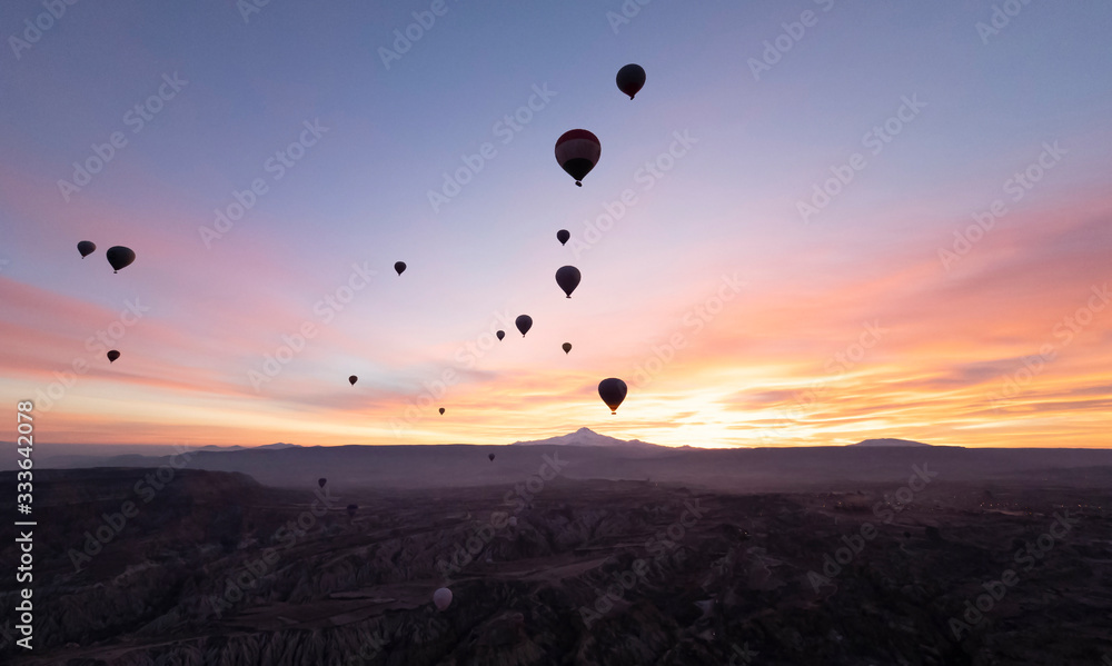 View of a volcano Mount Kayseri and silhouette of balloons seen from Goreme, Cappadocia with beautiful sunrise and colourful, golden, orange, pink and blue sky. It's fun, excited and impress activity 