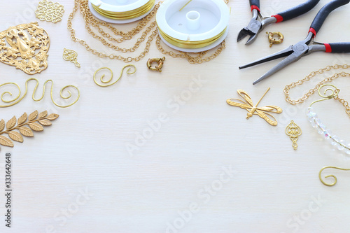 Jewellery making concept with gold chain, filigree charms and tools over white wooden background