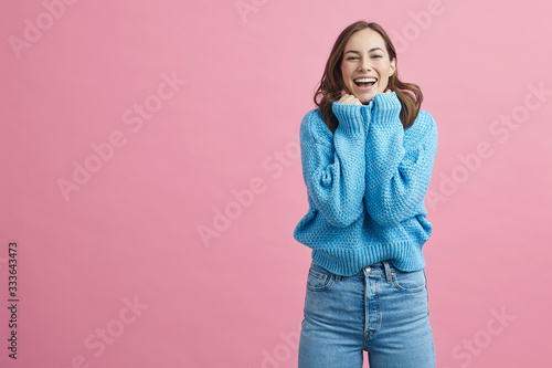 Portrait of happy and lovely young woman in a blue winter sweater on a pink background