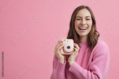 All pink concept with attractive girl holding a polaroid camera smiling to the viewer photo