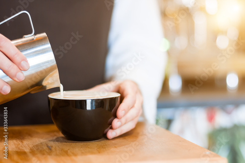 Closeup of female hands holding metal jug with hot milk and froth. Process of preparing  brewing americano  latte  capuchino. Barista woman is making coffee in cafe. Hot drinks  beverages concept.