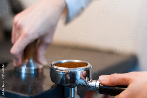 Barista woman is preparing  making espresso americano using professional machine  special tool kit in cafe. Closeup female hands are tempering  pressing ground coffee in metal portafilter.