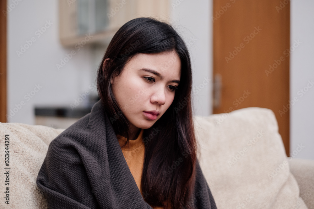 Portrait of Young woman sitting on a couch, holding her head, having a strong headache. Pandemic 2019 Coronavirus 2019-nCoV Concept. Portrait of Young woman sitting on a couch, holding her head, having a strong headache. Pandemic 2019 Coronavirus 2019-nCoV Concept.