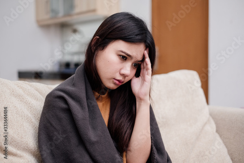 Portrait of Young woman sitting on a couch, holding her head, having a strong headache. Pandemic 2019 Coronavirus 2019-nCoV Concept.