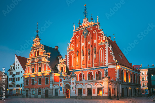 Riga, Latvia. Schwabe House And House Of The Blackheads At Town Hall Square, Ancient Historical Landmark And Popular Touristic Showplace In Summer Evening. Night Illuminations
