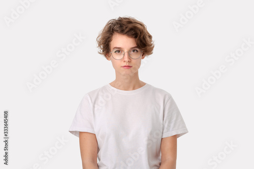 Concerned young woman in a white shirt and eyeglasses looking positively into a camera photo