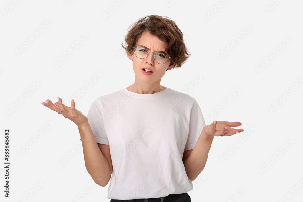 Clueless young woman in a white shirt and eyeglasses shrugging shoulders being at loss.