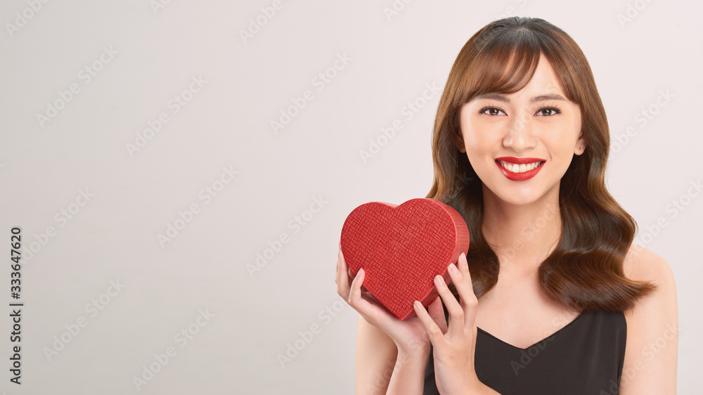 Cute young woman holding pink heart symbol against pale white background Cute young woman holding pink heart symbol against pale white background