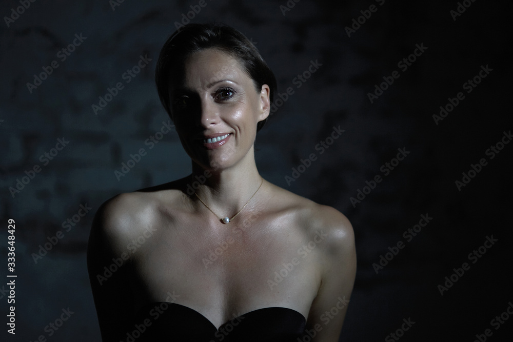 Half-naked sexy woman smiles beautifully at the camera in a dark room.