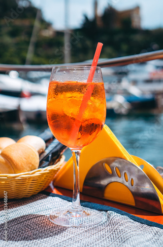 Close-up of the glass of refreshing Aperol Spritz cocktail during aperitif time in Portofino, one of the most popular picturesque coastal villages on the Italian Riviera. 